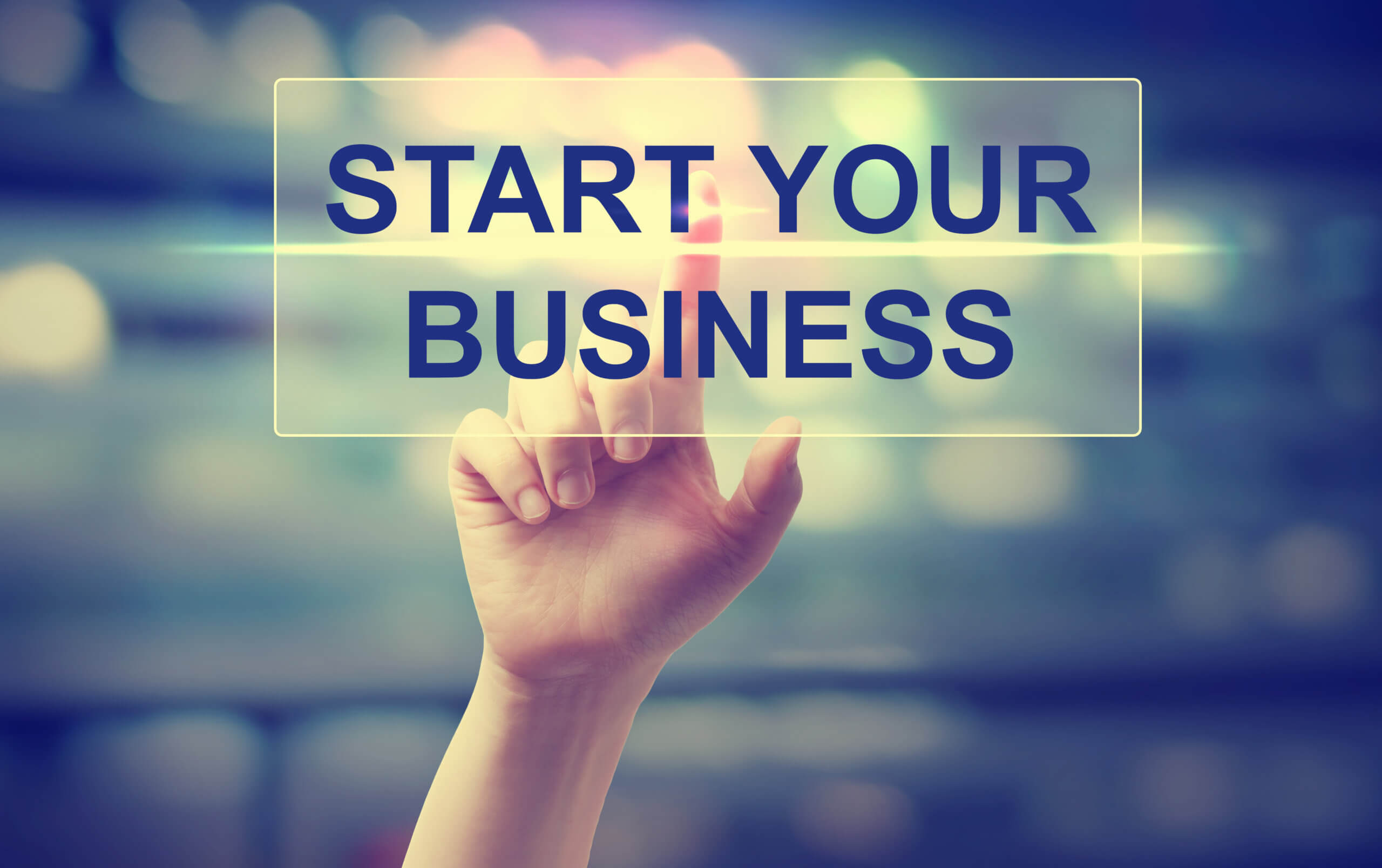 Hand pressing Start Your Business on blurred cityscape background